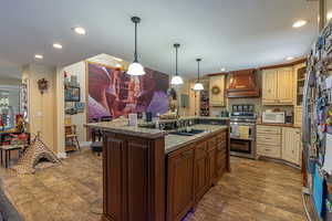 Kitchen with a kitchen island with sink, stainless steel range, dark wood-type flooring, sink, and premium range hood