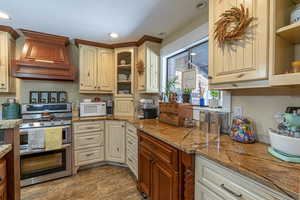 Kitchen featuring range with two ovens, wood-type flooring, custom exhaust hood, light stone countertops, and a textured ceiling