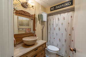 Bathroom with a textured ceiling, walk in shower, vanity, and toilet