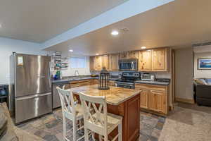 Kitchen featuring sink, a textured ceiling, stainless steel appliances, a kitchen breakfast bar, and a center island