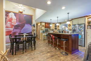 Kitchen with ceiling fan, wood-type flooring, decorative light fixtures, stainless steel refrigerator, and a kitchen bar