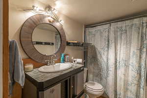 Bathroom with ceiling fan, toilet, curtained shower, vanity, and a textured ceiling