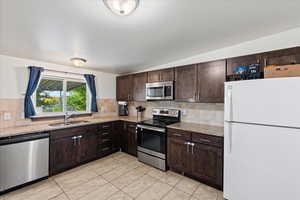 Kitchen with light stone countertops, appliances with stainless steel finishes, sink, and dark brown cabinets