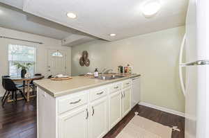 Kitchen featuring kitchen peninsula, sink, white appliances, white cabinetry, and dark hardwood / wood-style floors