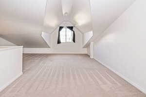 Additional living space with light carpet and vaulted ceiling