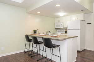 Kitchen featuring white appliances, dark hardwood / wood-style floors, kitchen peninsula, and white cabinetry