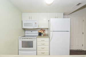 Kitchen featuring a textured ceiling, dark wood-type flooring, white appliances, and white cabinets