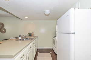 Kitchen with white cabinets, sink, white appliances, a textured ceiling, and dark hardwood / wood-style flooring