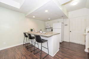 Kitchen with white cabinets, kitchen peninsula, white appliances, dark hardwood / wood-style floors, and a breakfast bar area