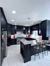 Kitchen featuring custom range hood, hanging light fixtures, appliances with stainless steel finishes, and kitchen breakfast bar