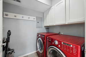 Washroom with light tile patterned flooring, electric panel, washer and dryer, and cabinets