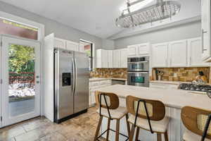 Kitchen with decorative backsplash, white cabinets, appliances with stainless steel finishes, and a kitchen breakfast bar