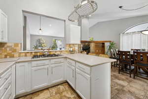 Kitchen with pendant lighting, kitchen peninsula, white cabinetry, and decorative backsplash