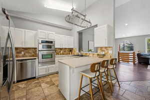 Kitchen featuring a breakfast bar, vaulted ceiling, stainless steel appliances, kitchen peninsula, and white cabinets