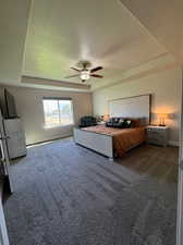 Carpeted bedroom featuring ceiling fan, a tray ceiling, and a textured ceiling