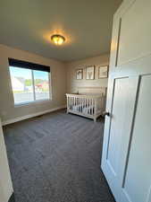 Unfurnished bedroom with dark carpet and a nursery area