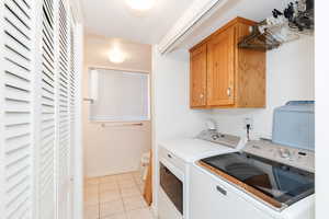 Washroom with independent washer and dryer, light tile patterned flooring, cabinets, and a textured ceiling