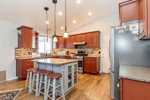 Kitchen featuring light hardwood / wood-style flooring, stainless steel appliances, lofted ceiling, and a kitchen island