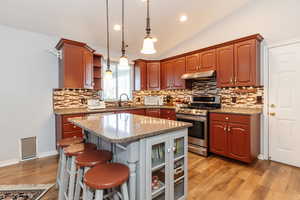 Kitchen with hanging light fixtures, stainless steel range with gas stovetop, vaulted ceiling, light stone countertops, and light hardwood / wood-style floors