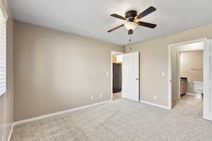 Unfurnished bedroom with ceiling fan, ensuite bath, and light carpet