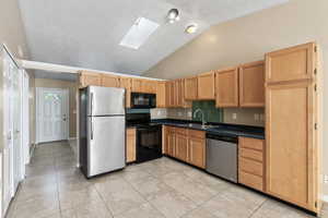 Kitchen with high vaulted ceiling, black appliances, sink, light tile patterned flooring, and a skylight