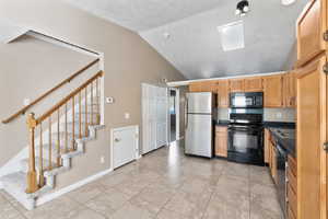 Kitchen with light tile patterned flooring, black appliances, and vaulted ceiling with skylight