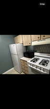 Kitchen with light brown cabinets, backsplash, extractor fan, white gas range, and stainless steel refrigerator