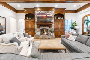 Living room with ornamental molding, a stone fireplace, and wood-type flooring