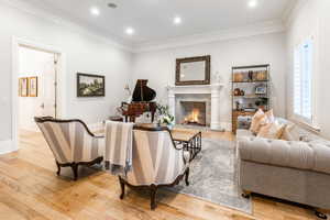 Living room with light wood-type flooring, a fireplace, and ornamental molding