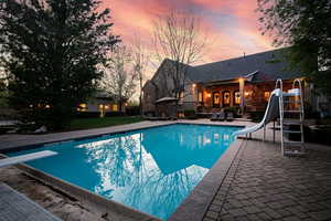 Pool at dusk featuring a diving board, a water slide, and a patio area