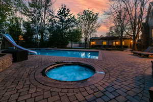 Pool at dusk featuring an in ground hot tub, a water slide, and a patio