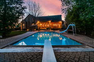 Pool at dusk with a diving board, a water slide, and a patio area