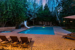 Pool at dusk featuring a patio, a water slide, and a diving board