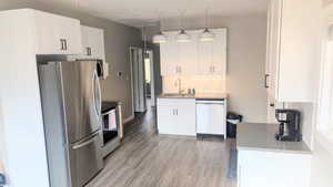 Kitchen featuring white cabinetry, sink, stainless steel appliances, decorative light fixtures, and light wood-type flooring