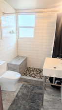 Bathroom with tiled shower, tile patterned flooring, toilet, and tile walls