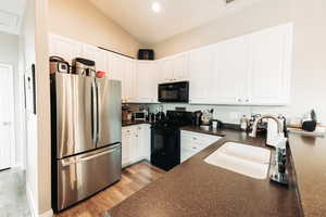 Kitchen with light hardwood / wood-style flooring, sink, lofted ceiling, black appliances, and white cabinetry