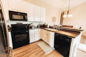 Kitchen featuring kitchen peninsula, decorative light fixtures, light hardwood / wood-style flooring, black appliances, and a notable chandelier