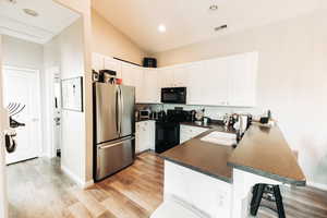 Kitchen featuring sink, kitchen peninsula, black appliances, a kitchen bar, and white cabinetry