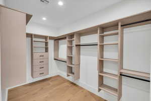 Walk in closet with light hardwood / wood-style floors