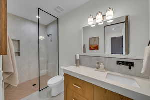 Bathroom featuring backsplash, vanity, toilet, and a tile shower