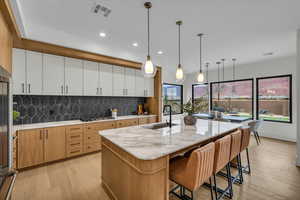 Kitchen with sink, a center island with sink, pendant lighting, stainless steel gas stovetop, and white cabinets