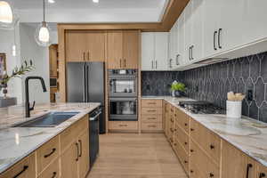 Kitchen featuring pendant lighting, white cabinetry, sink, black appliances, and light stone countertops