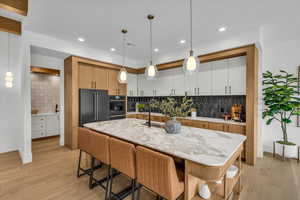 Kitchen featuring white cabinets, hanging light fixtures, black appliances, light stone countertops, and a center island with sink