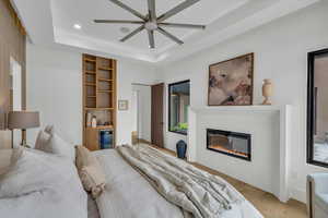 Bedroom with ceiling fan, beverage cooler, a tray ceiling, and light hardwood / wood-style flooring