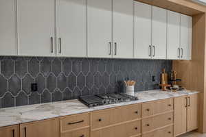 Kitchen featuring white cabinetry, light stone countertops, stainless steel gas cooktop, and decorative backsplash