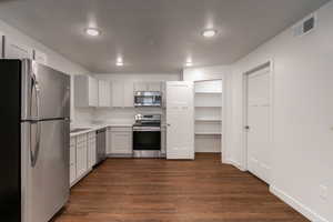 Kitchen featuring sink, appliances with stainless steel finishes, dark hardwood / wood-style flooring, and white cabinetry