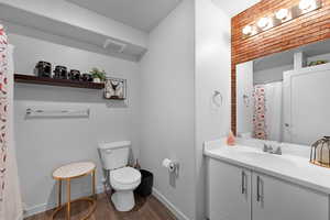 Bathroom featuring wood-type flooring, brick wall, vanity, and toilet