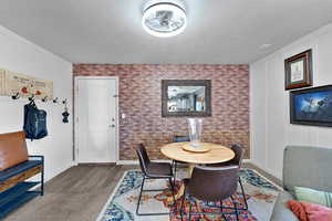 Dining room with brick wall, a textured ceiling, wood-type flooring, and ceiling fan