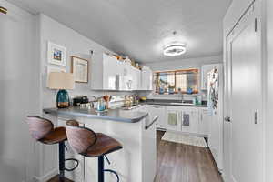 Kitchen featuring white appliances, dark hardwood / wood-style flooring, kitchen peninsula, white cabinets, and a kitchen bar