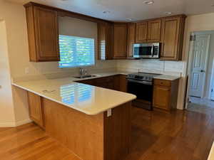 Kitchen featuring lhardwood flooring, black / electric stove, sink, kitchen peninsula, and backsplash